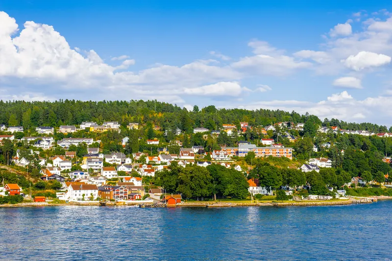 Hvite og fargerike hus i skogkledd li ned mot fjorden i Bærum